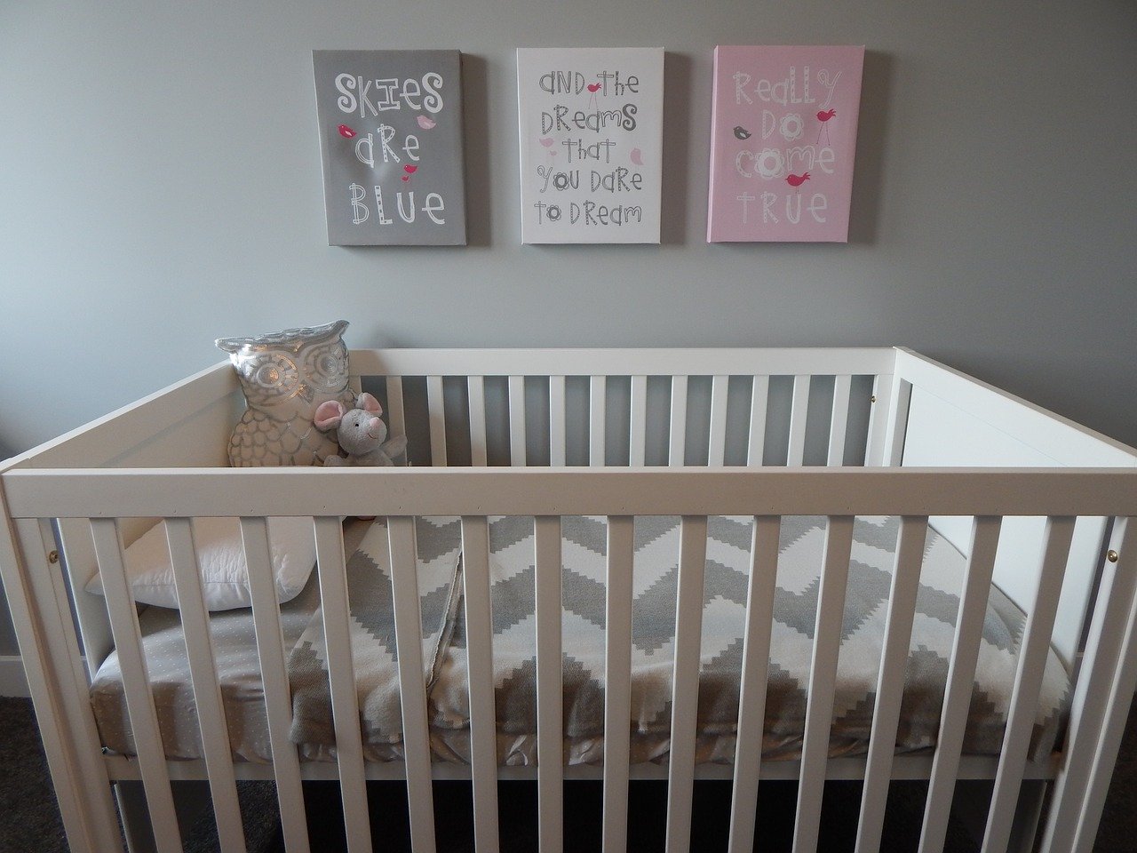 chambre bébé avec lit à barreaux et cadres au dessus et peluche dans le lit